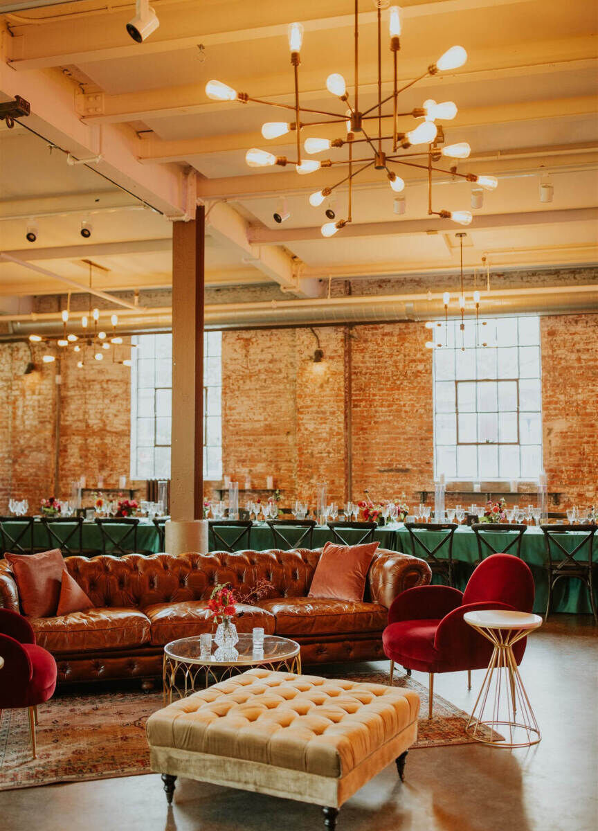 Industrial Wedding Venues: A couch and chair under an industrial chandelier with a brick wall and table behind it.