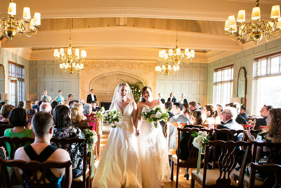 LGBTQ Wedding Ideas: Two brides smiling and holding hands while exiting their wedding ceremony.