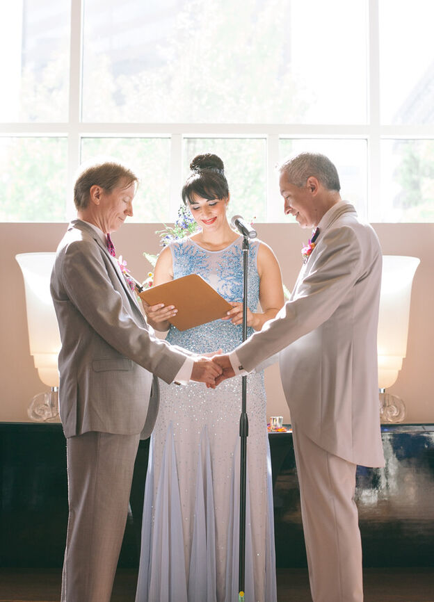 LGBTQ Wedding Ideas: Two grooms holding hands and their officiant during the wedding ceremony.