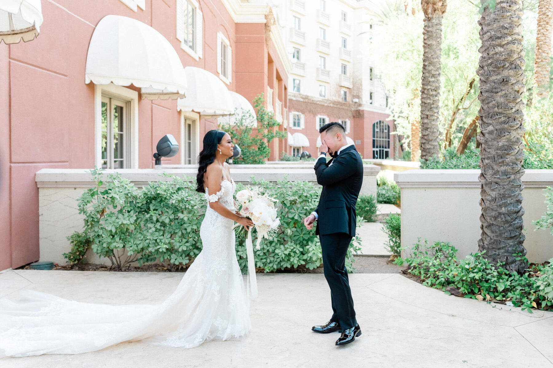 Marriott Weddings: A groom wiping his eyes during an emotional first look with the bride at a property with pink exterior walls and palm trees around them.