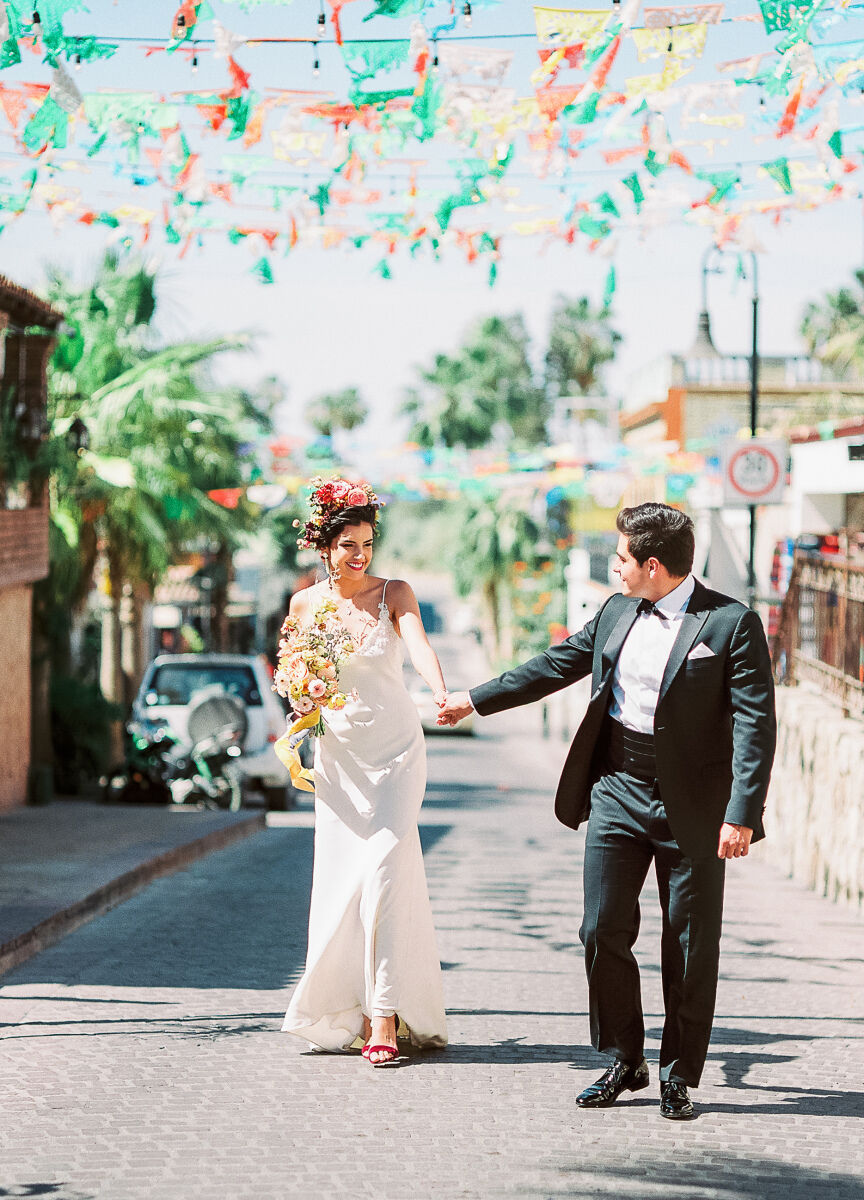 Mexican wedding: couple walking hand in hand down the streets of Mexico with colorful flags strung overhead 