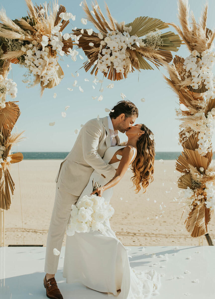Mexican wedding: couple kissing under their neutral wedding arch on the beach