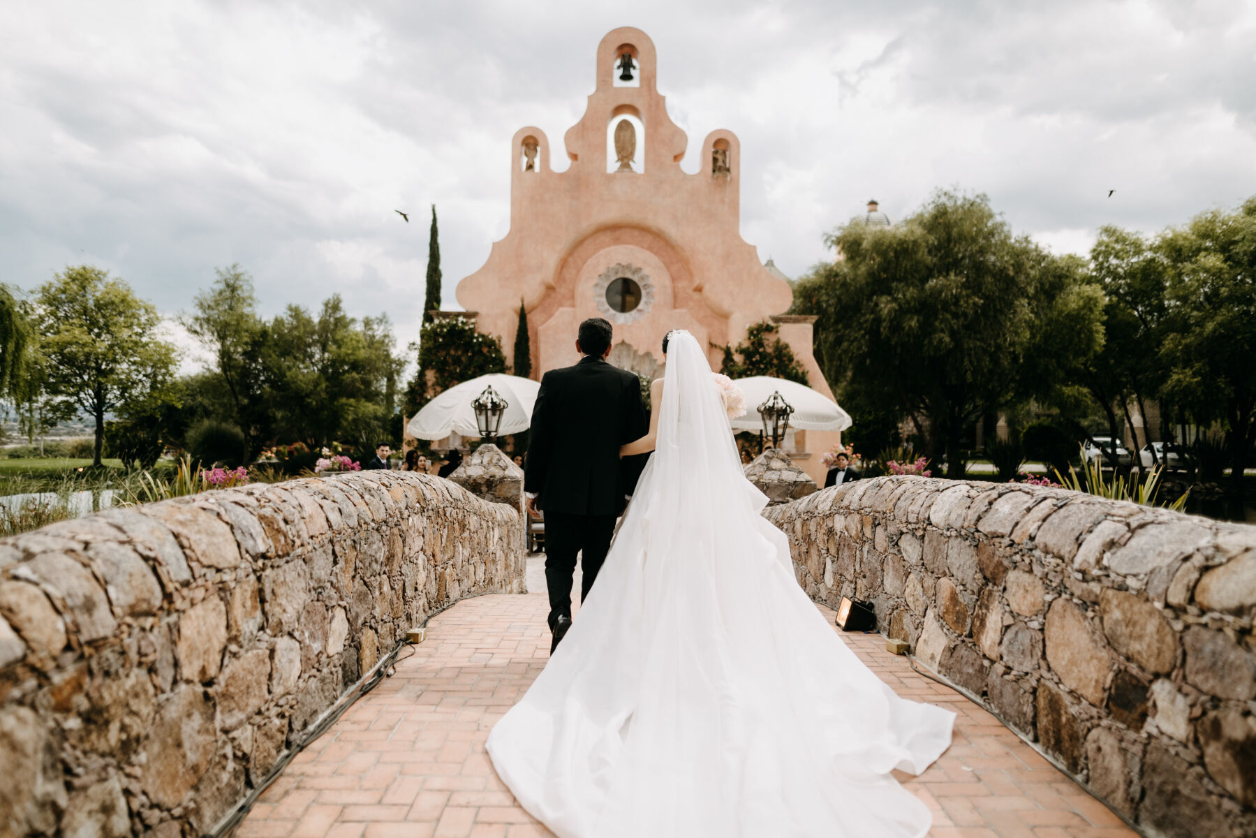 Mexican wedding: couple walking across stone bride to adobe style church