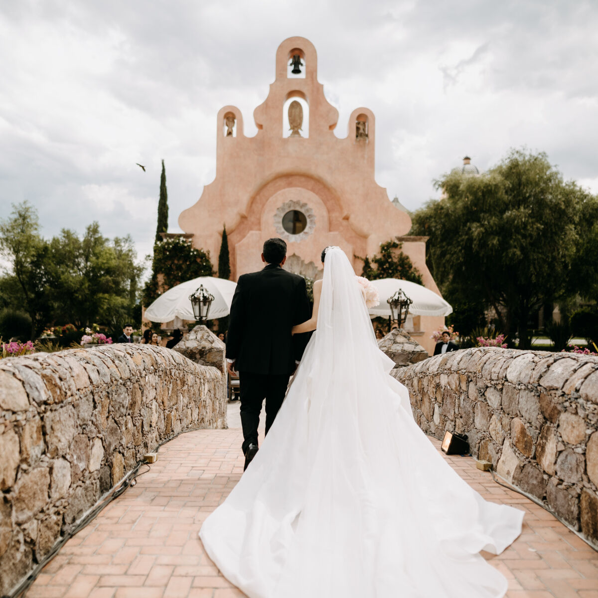 Mexican wedding: couple walking across stone bride to adobe style church