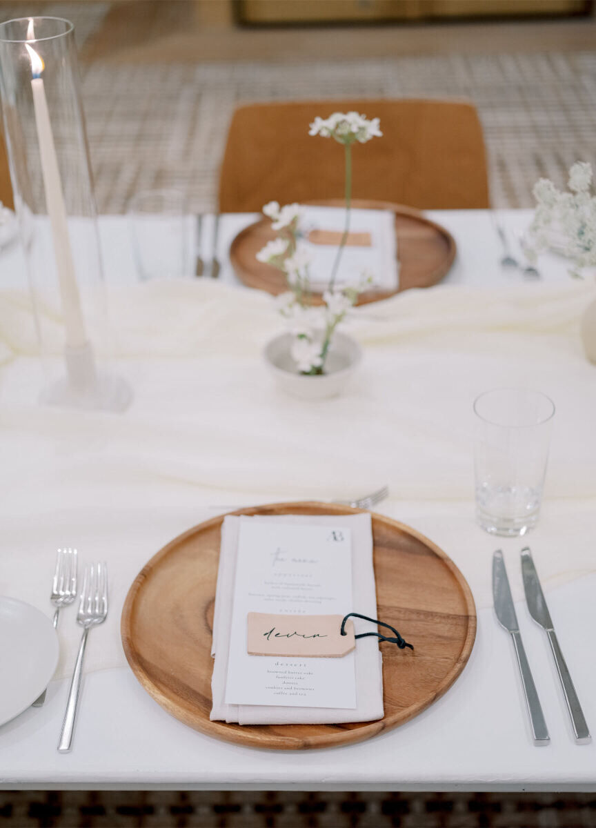 Wood chargers held cream napkins, simple menus, and personalized leather tags that served as place cards at this modern California wedding reception.
