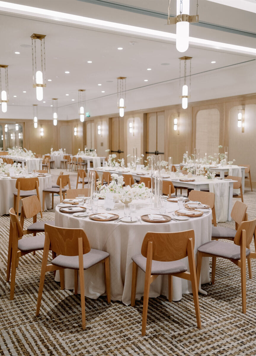 A modern California wedding reception, with a mix of round and long tables set in shades of white and tones of wood.