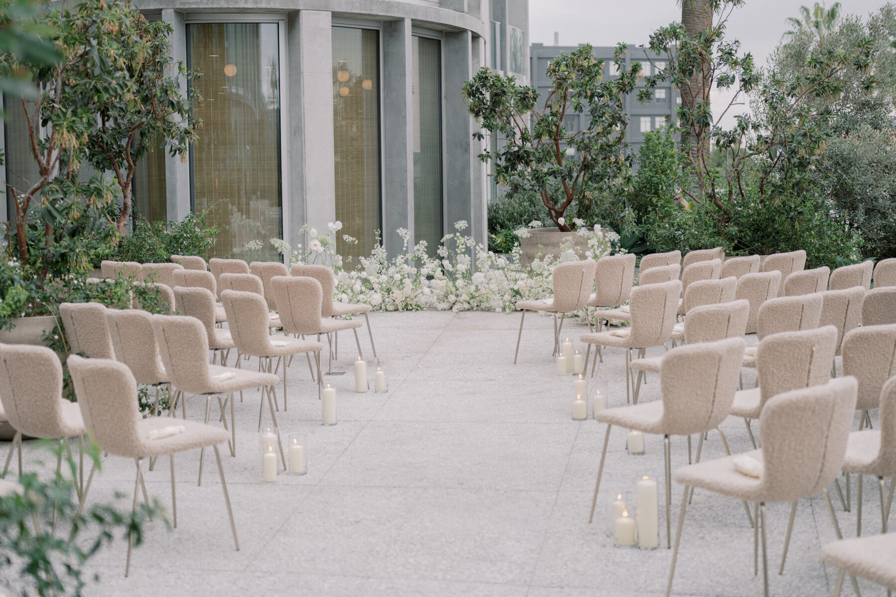 The outdoor ceremony of a modern California wedding featured textured taupe chairs and a low, rounded floral installation to delineate where the couple and their officiant would stand.