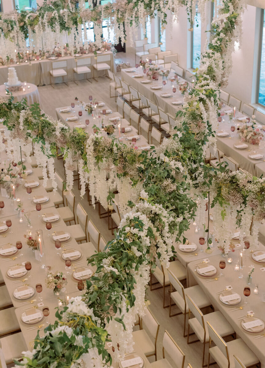 An overhead view of a modern fairytale wedding reception, inside D'vine Grace Vineyard's event space, with greenery and flowers hanging over the long tables.
