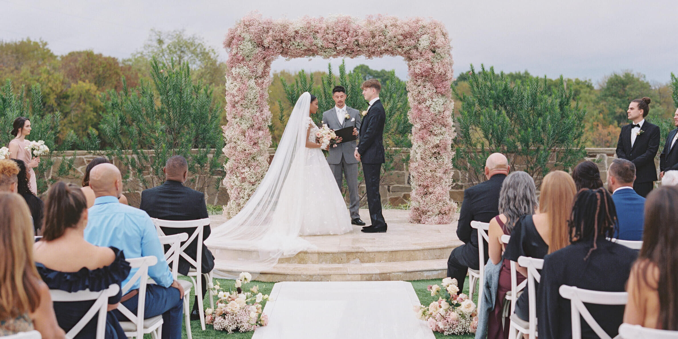A modern fairytale wedding ceremony, with the bride and groom standing under an arch of pink baby's breath.
