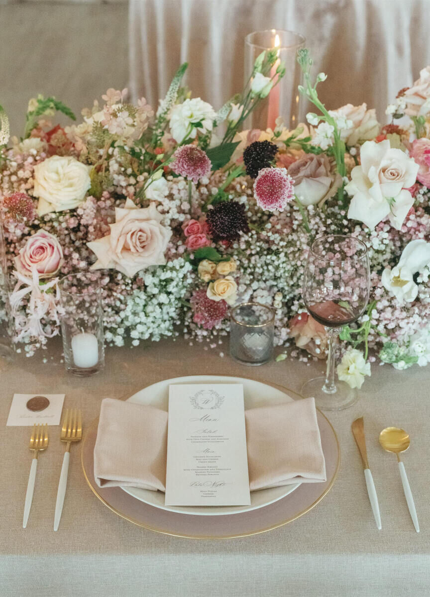 A placesetting at a modern fairytale wedding reception, with white-and-gold flatware and a gold-rimmed charger pairing with wax seal-embellished place cards and monogrammed menus.