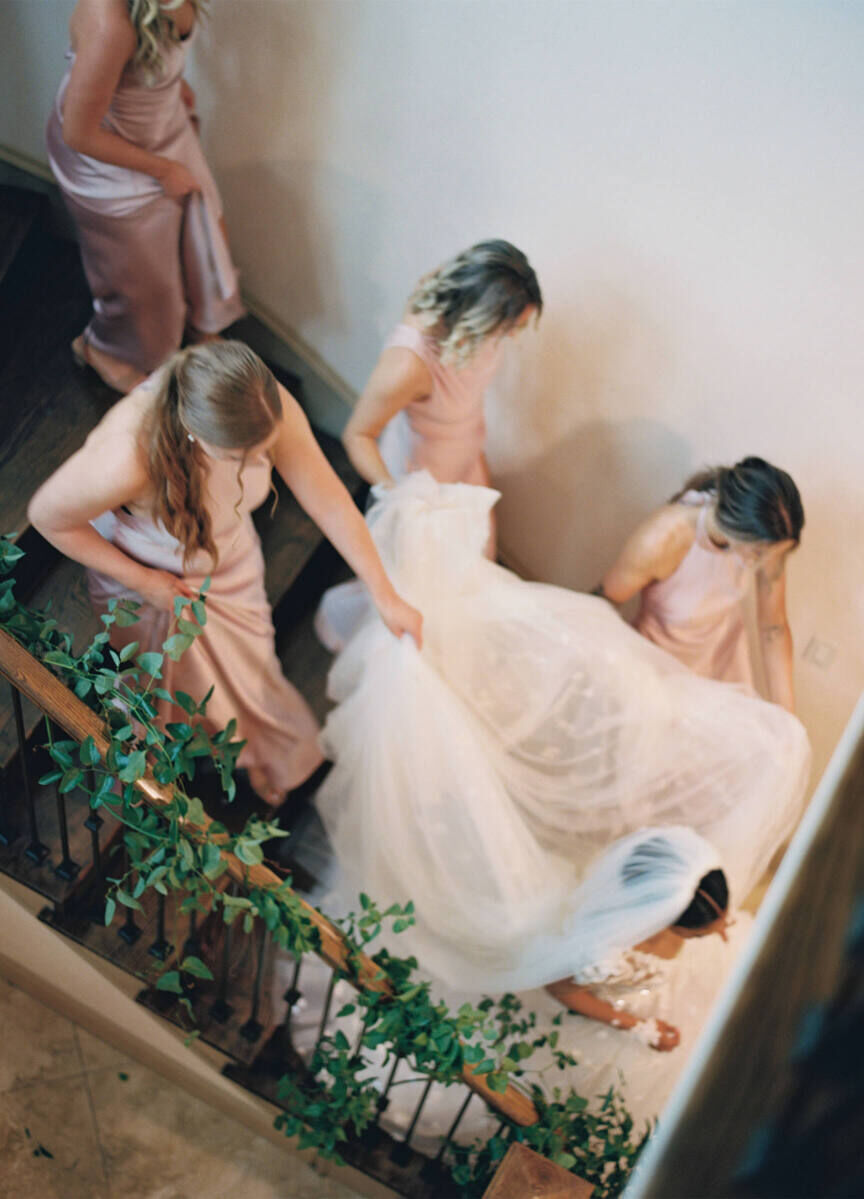 Bridesmaids in pink gowns escort the bride down the stairs to get to her modern fairytale wedding ceremony.