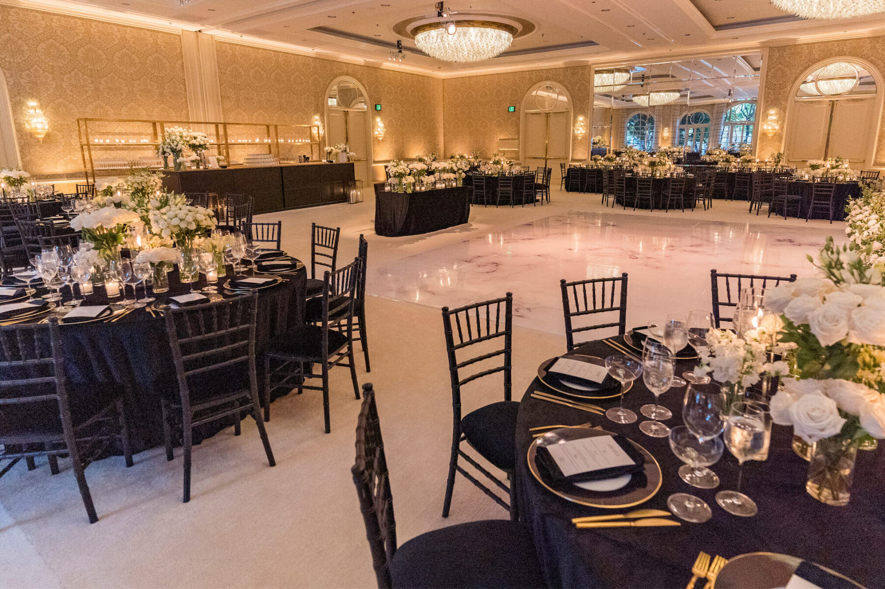 A ballroom set for a modern reception in a color palette of black and white, boasts a mix of tables and a marbled dance floor.