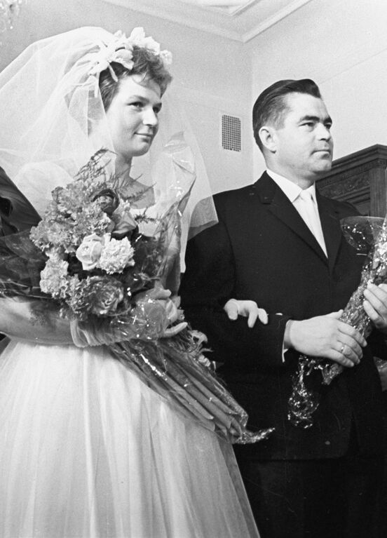 Most Influential Women in History Weddings: Valentina Tereshkova standing at the alter with husband Andrian Nikolaev, adorned in wedding gown and veil, holding large bouquet of wedding flowers