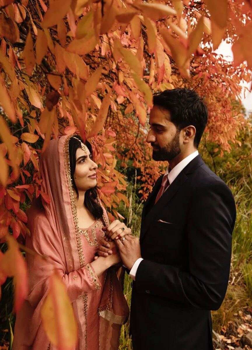 Most Influential Women in History Weddings: Malala Yousafzai posing with her husband Asser Malik under autumnal trees with leaves that match her rouge veil