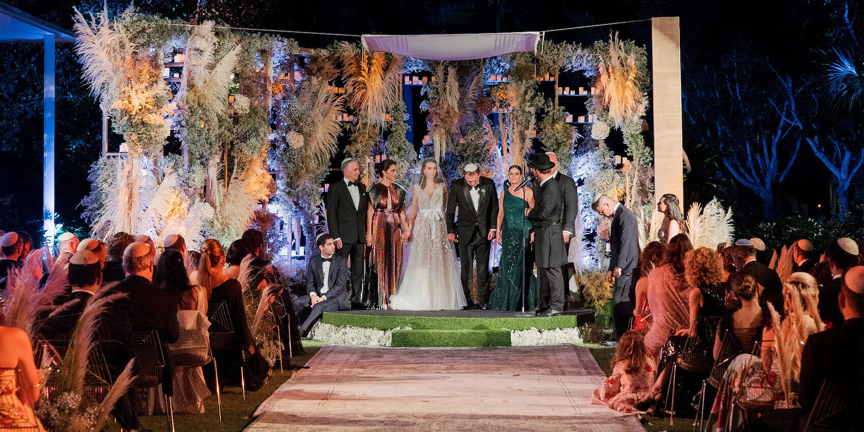 An evening ceremony of a museum wedding, with the pampas grass chuppah illuminated.