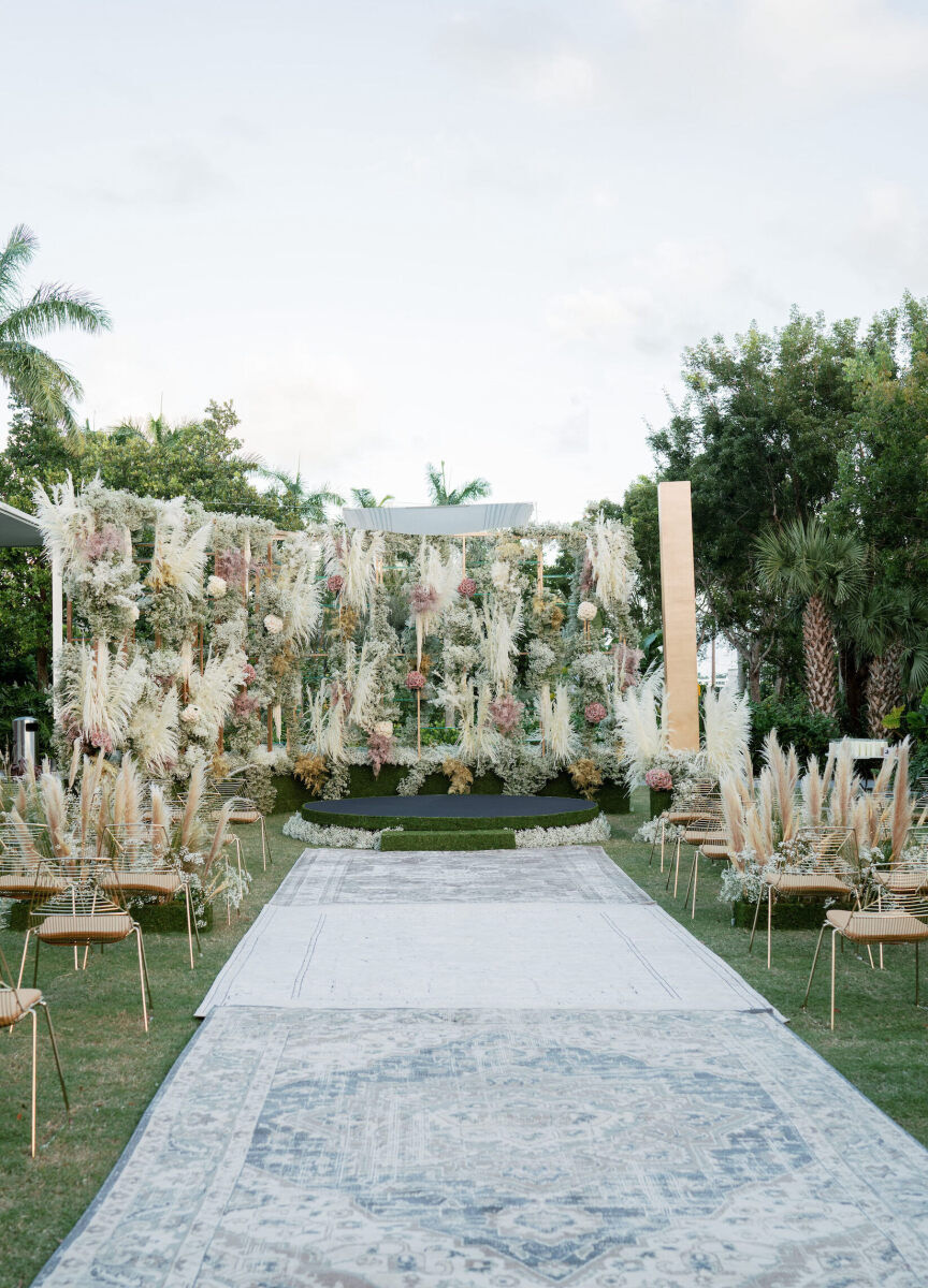 An outdoor ceremony setup at a museum wedding with rugs lining the aisle and a pampas grass installation behind the chuppah.