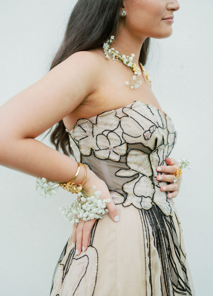 A bridesmaid wears gold jewelry with baby's breath flowers woven into it, instead of carrying a traditional bouquet.