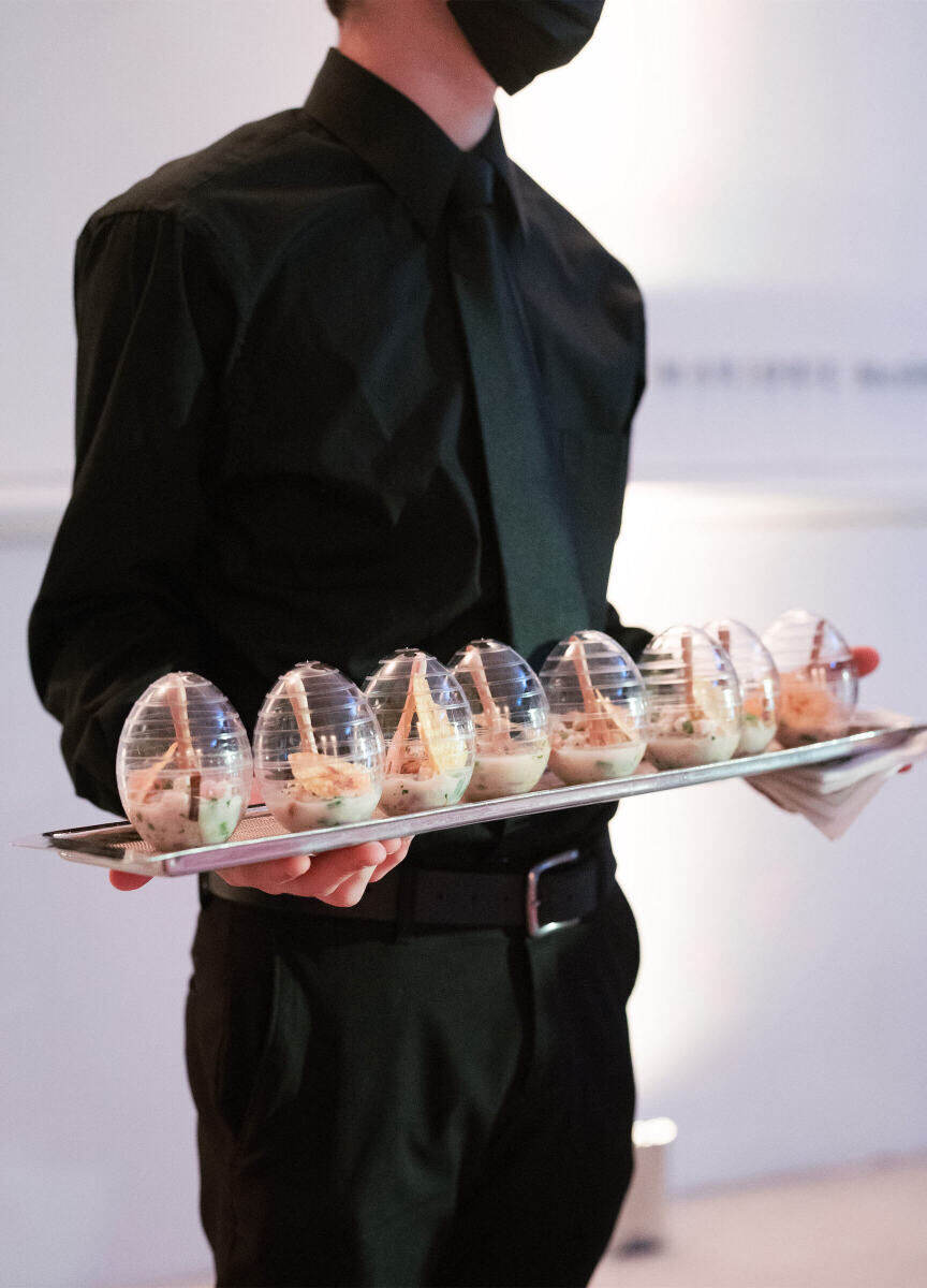 A server holds a tray of egg-shaped vessels with an appetizer in each.