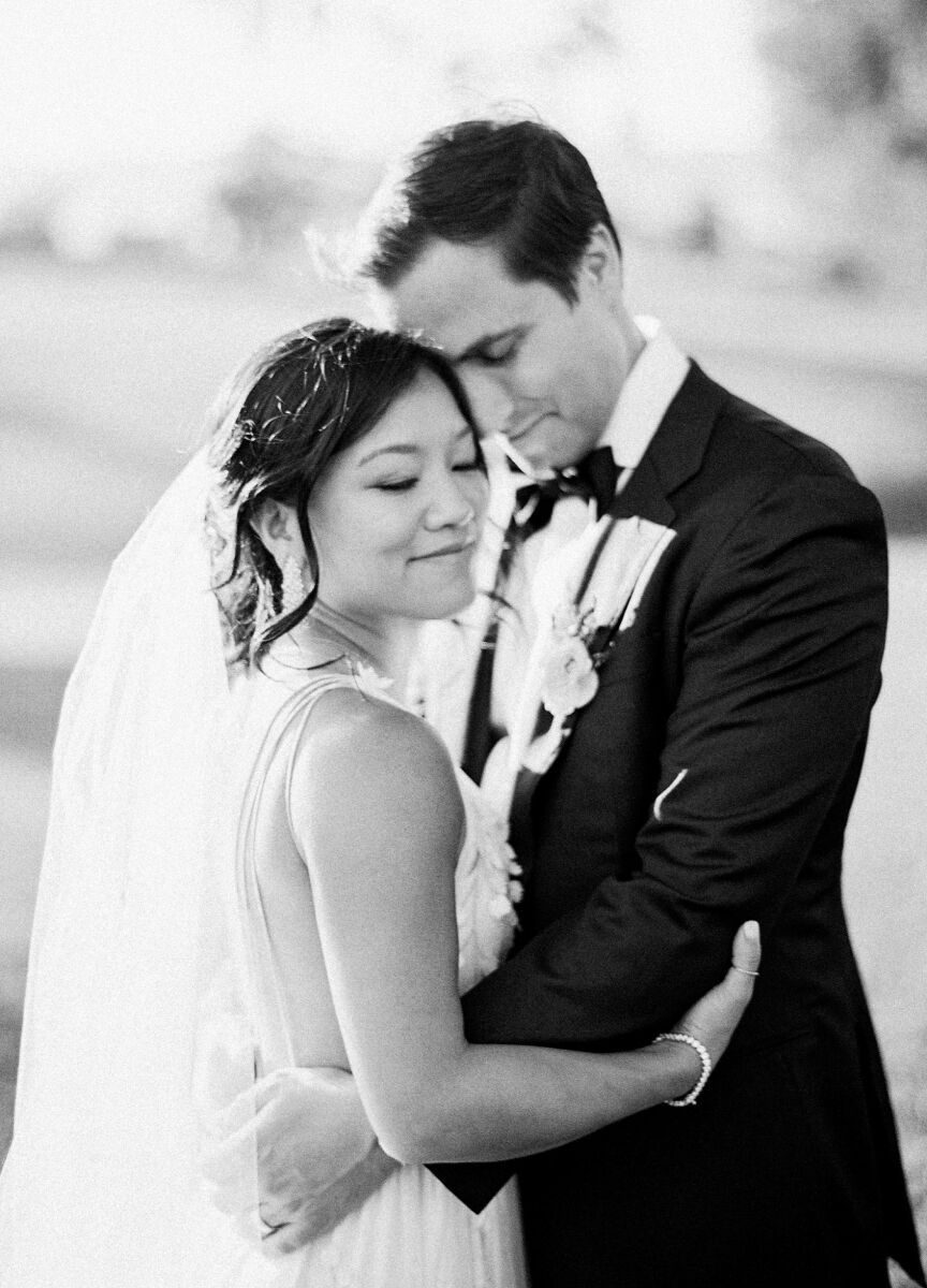 A black and white portrait of a bride and groom embracing, standing forehead to forehead.