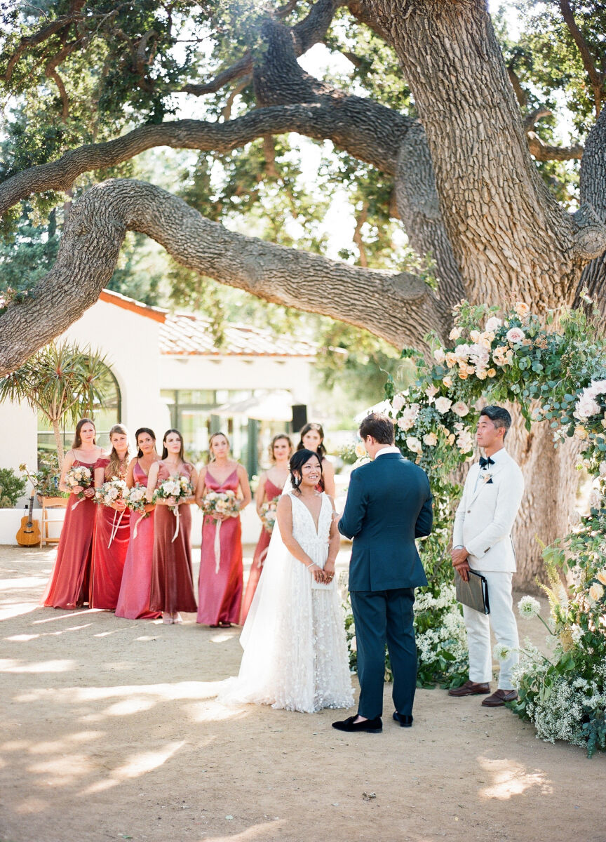 A side view of an outdoor wedding ceremony, showing the bridesmaids in pink dresses behind the bride.