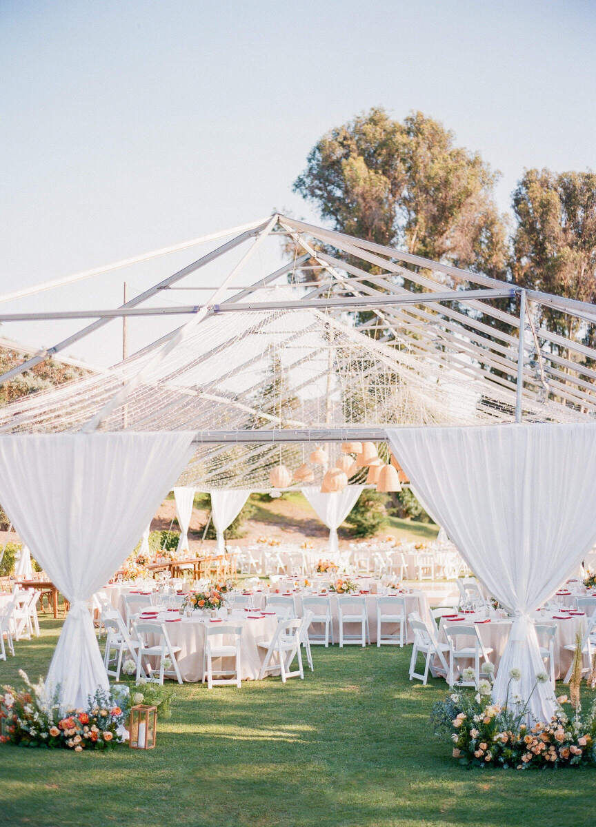 An open-air tented wedding reception with a mix of round and rectangular tables inside.