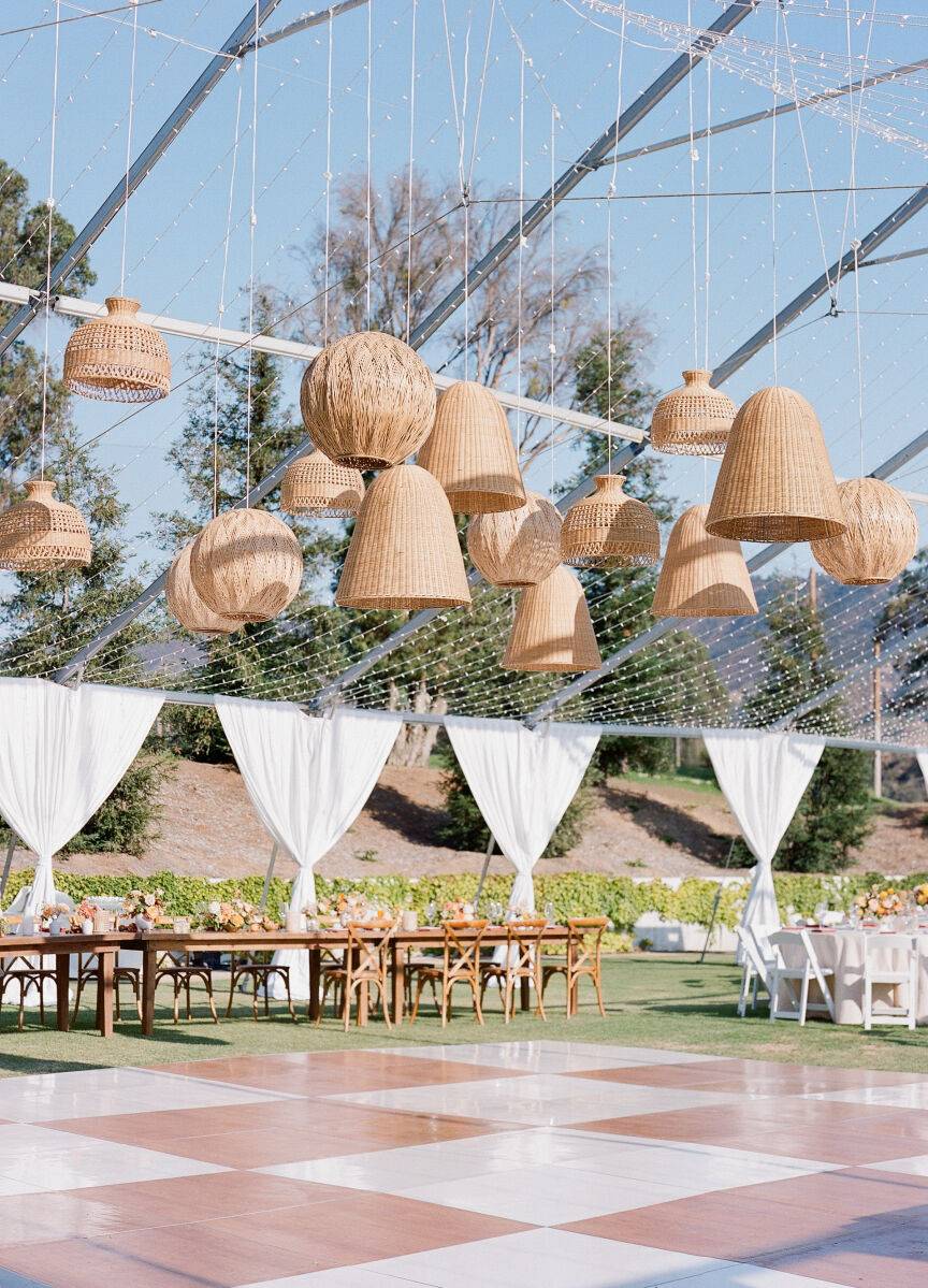 An open-air tent structure for a wedding reception included hanging rattan light fixtures over a checkerboard dance floor.