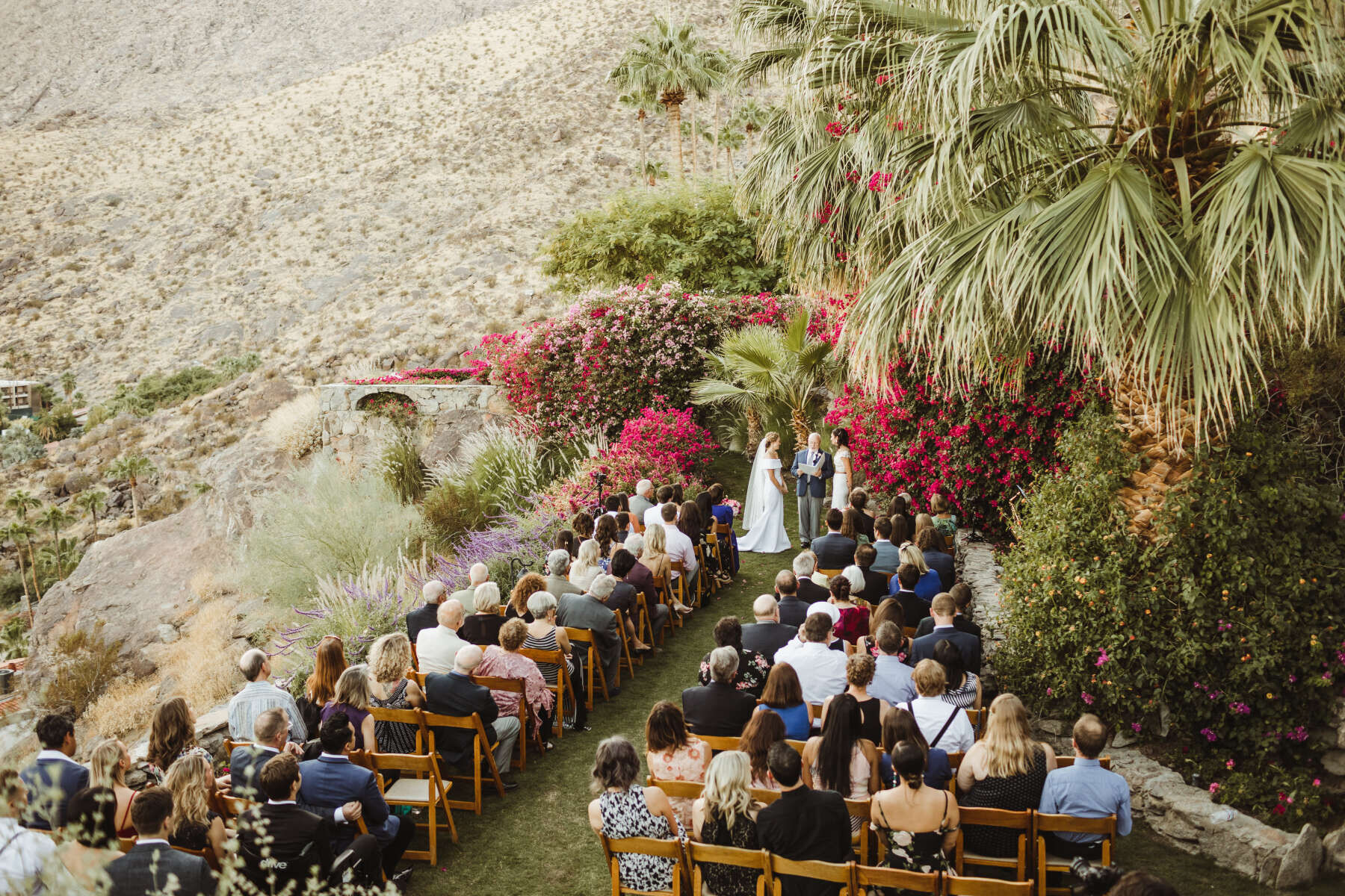 Pink Wedding: Two brides, their officiant, and guests at an outdoor ceremony in the California desert.