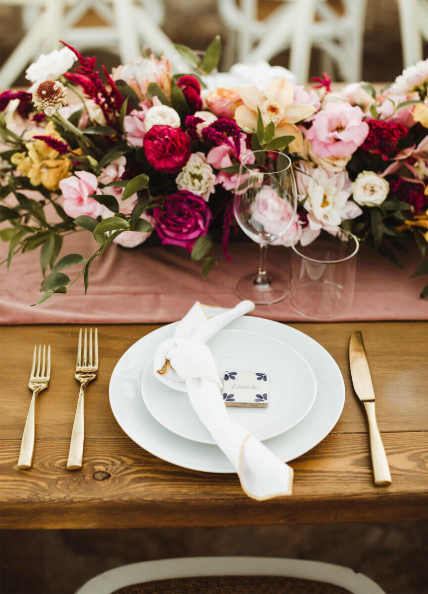 Pink Wedding: A brightly colored floral arrangement on a reception table set with gold flatware.