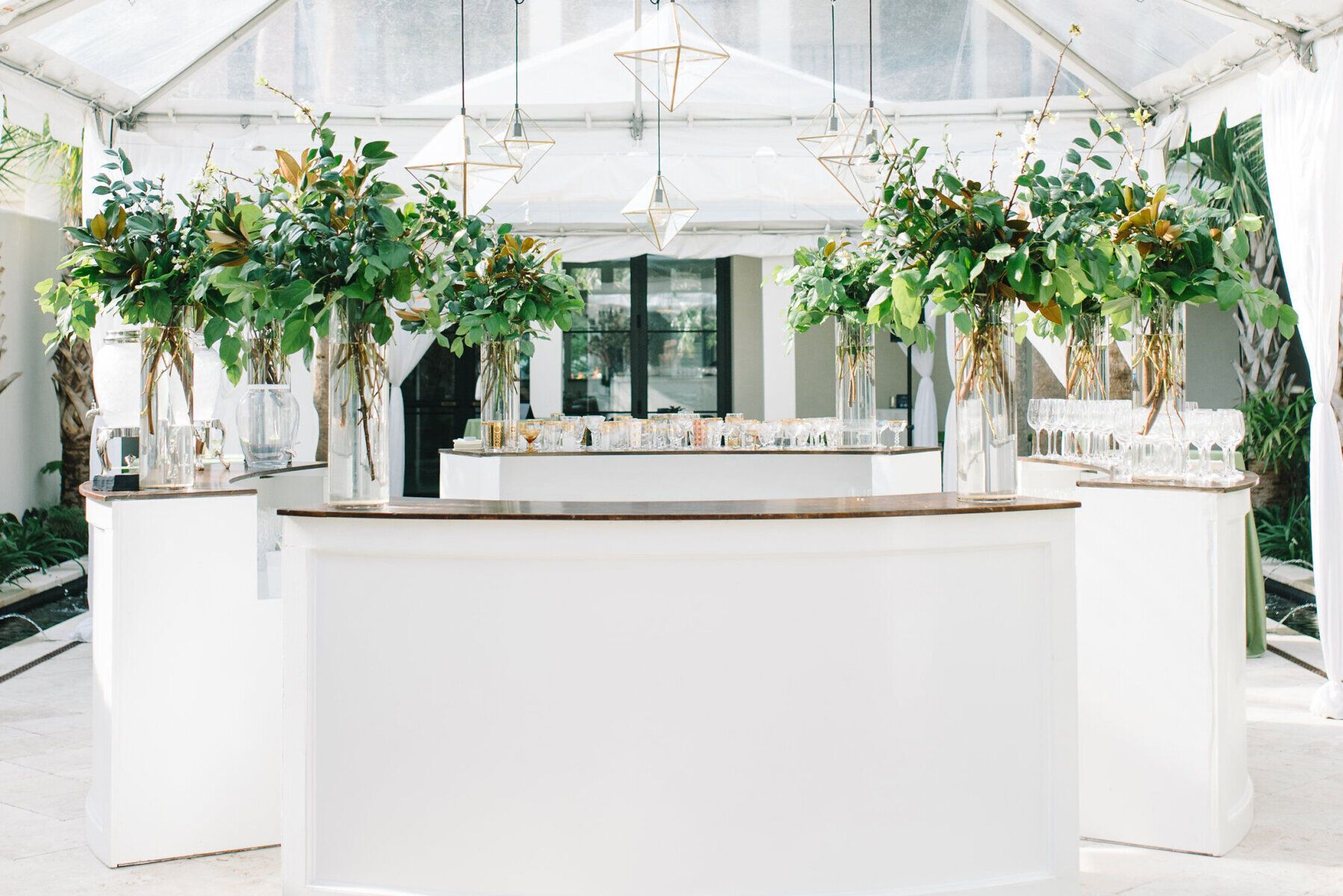 Tented Wedding Ideas: Inside of a tented wedding reception, clear-top tent with bright white bar accented with greenery bouquets 