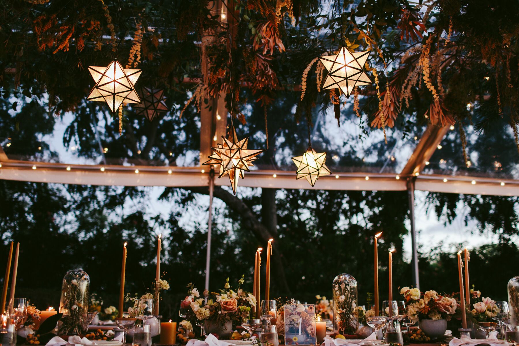 Tented Wedding Ideas: Inside of a tented wedding reception at dusk, featuring a clear-top tent with hanging geometric glowing lanterns 