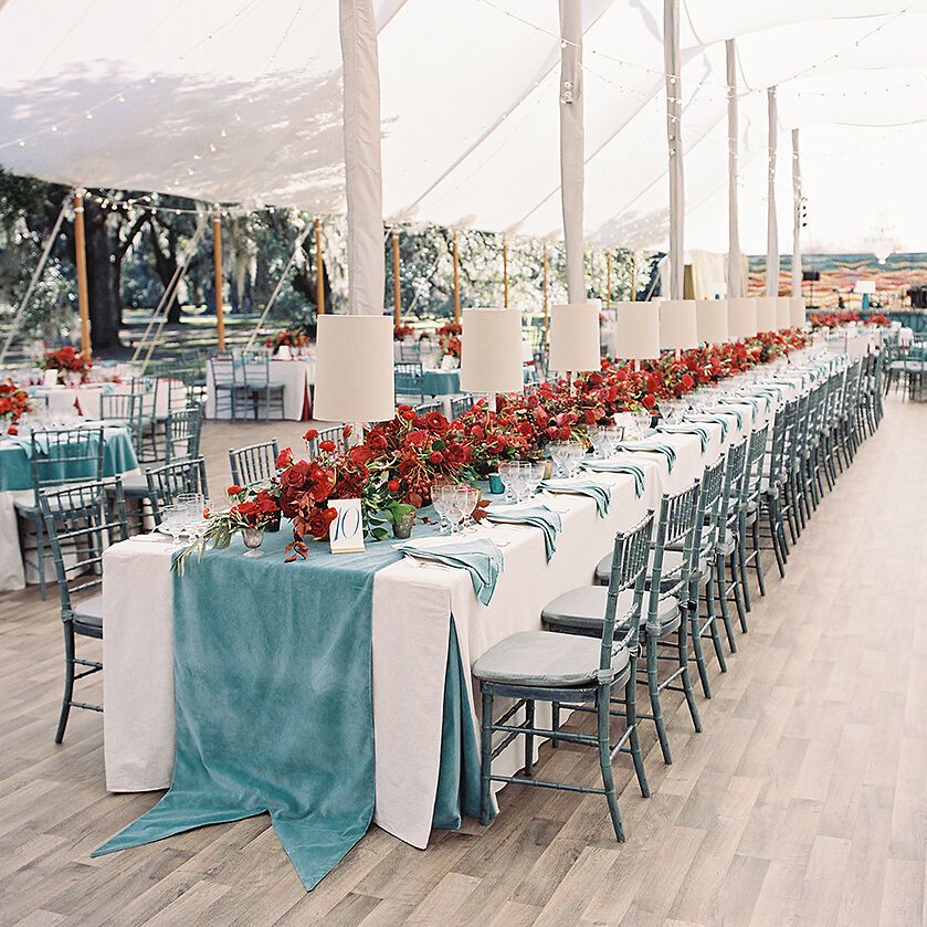 Wedding budget: Tented wedding reception with long table featuring a teal table runner and red floral decor