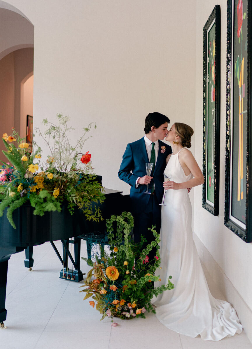 Large floral arrangements surround a piano in a private estate where a couple shares a kiss.