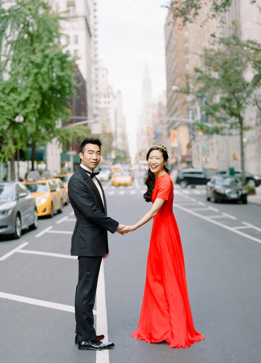 Bride wearing red wedding dress and couple holding hands in city street