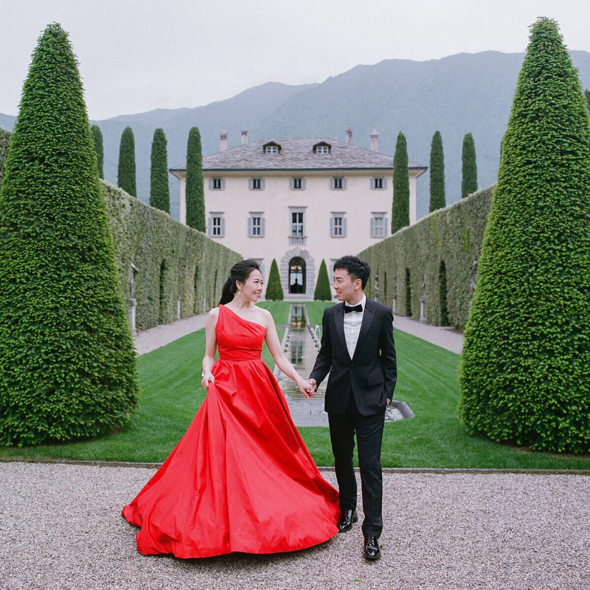 Bride in red wedding dress, wedding couple holding hands in front of an estate. 