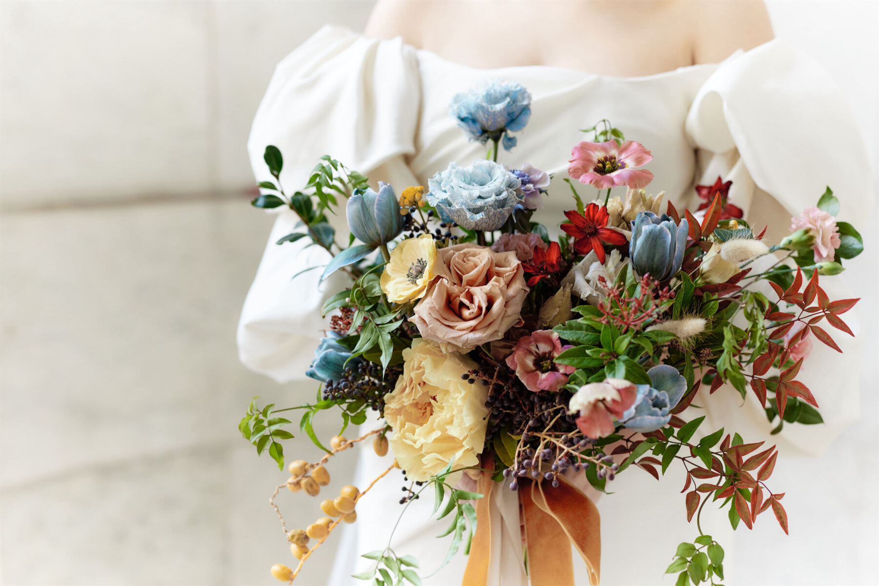 A colorful bridal bouquet made of tulips, roses, anemone, and berries.