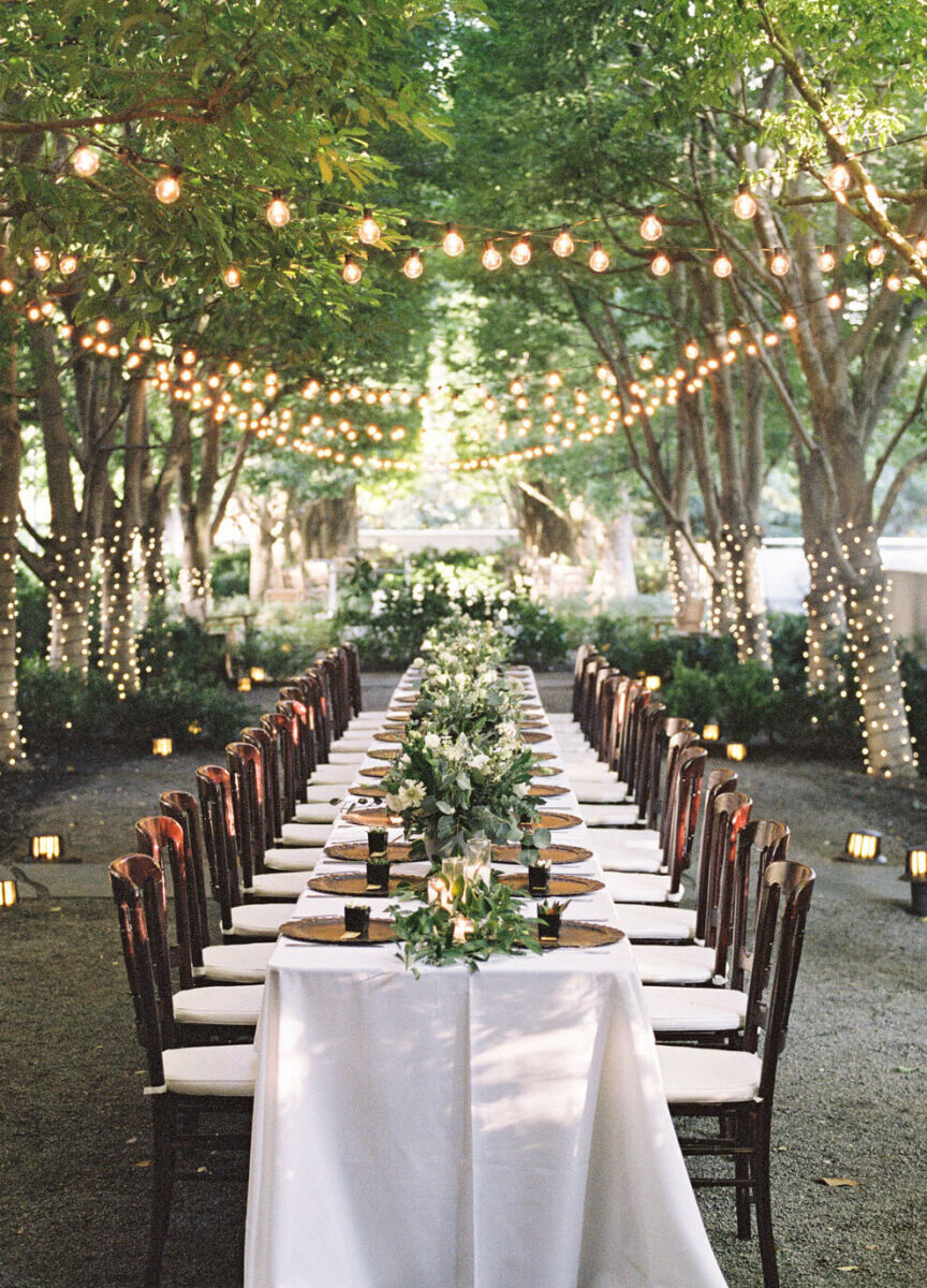 Restaurant Weddings: A long table set up for a reception at Marie Gabrielle in the garden with string lights overhead and trees lining the space.