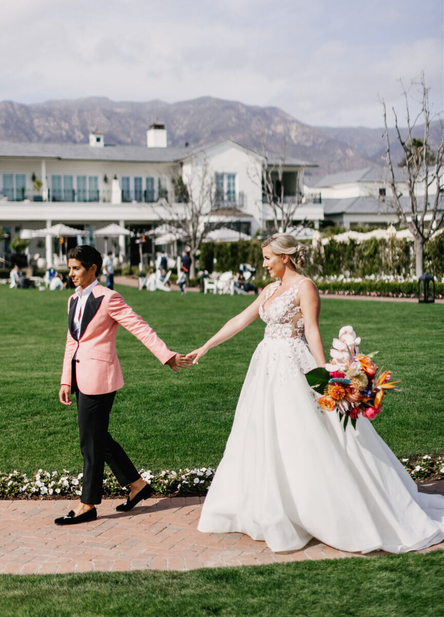 Romantic Wedding Venues: Two brides holding hands while walking down a path outside at Rosewood Miramar Beach in Montecito, California.
