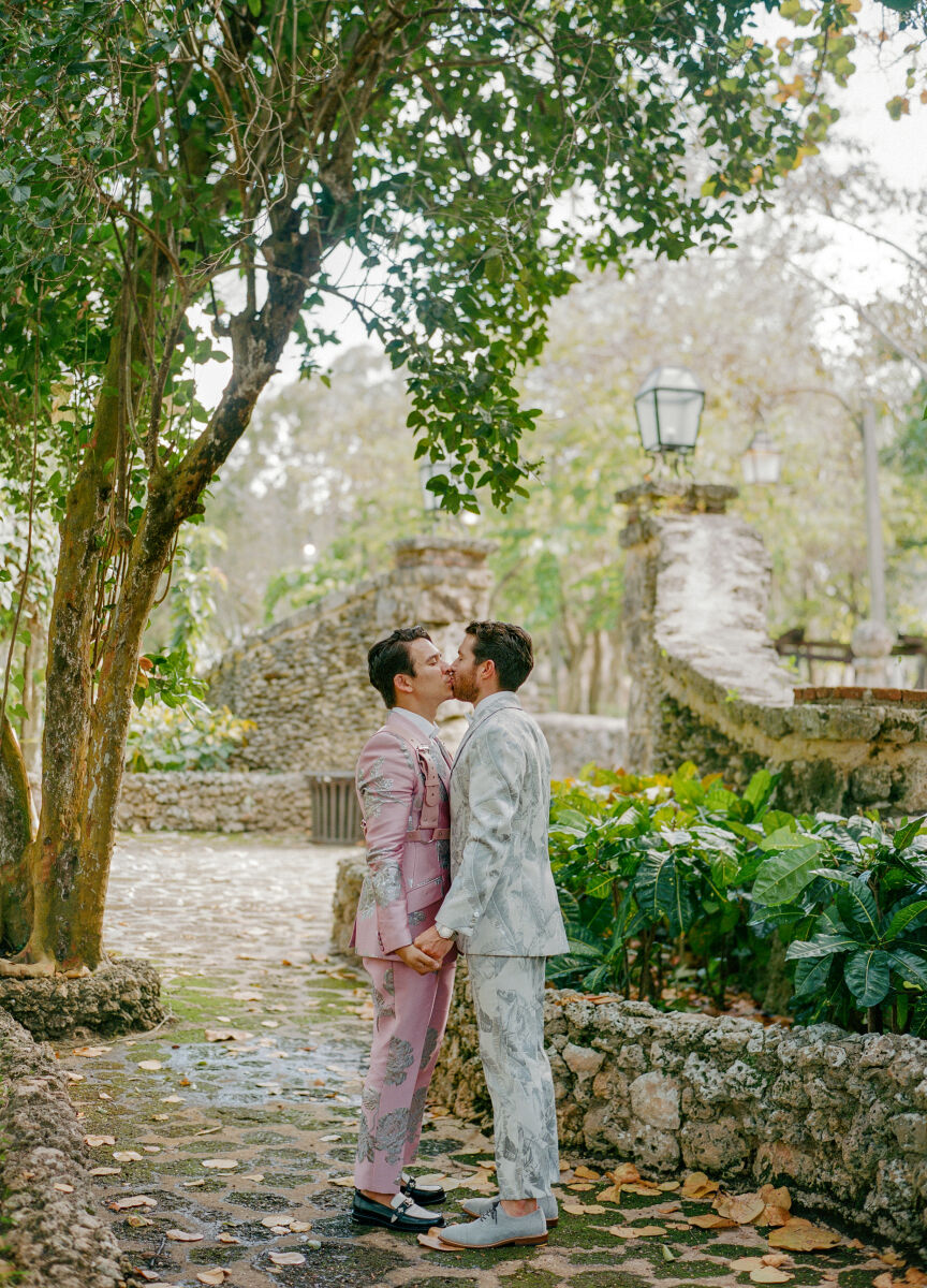 Romantic Wedding Venues: Two grooms sharing a kiss on a cobblestone path at Casa de Campo Resort & Villas.