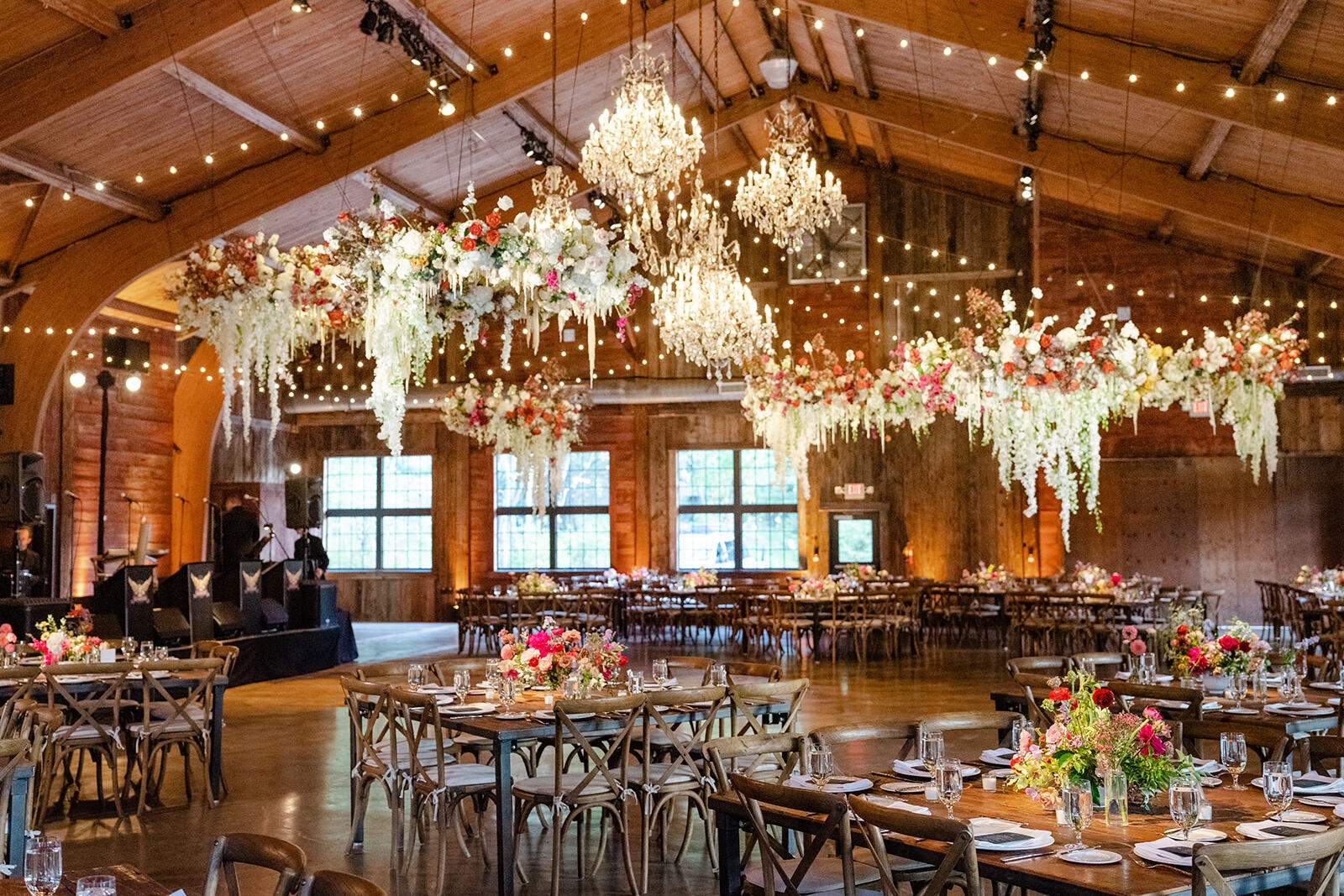 SEO for Wedding Venues: An indoor reception setup with chandeliers and hanging floral installations with wooden tables, chairs and flooring.