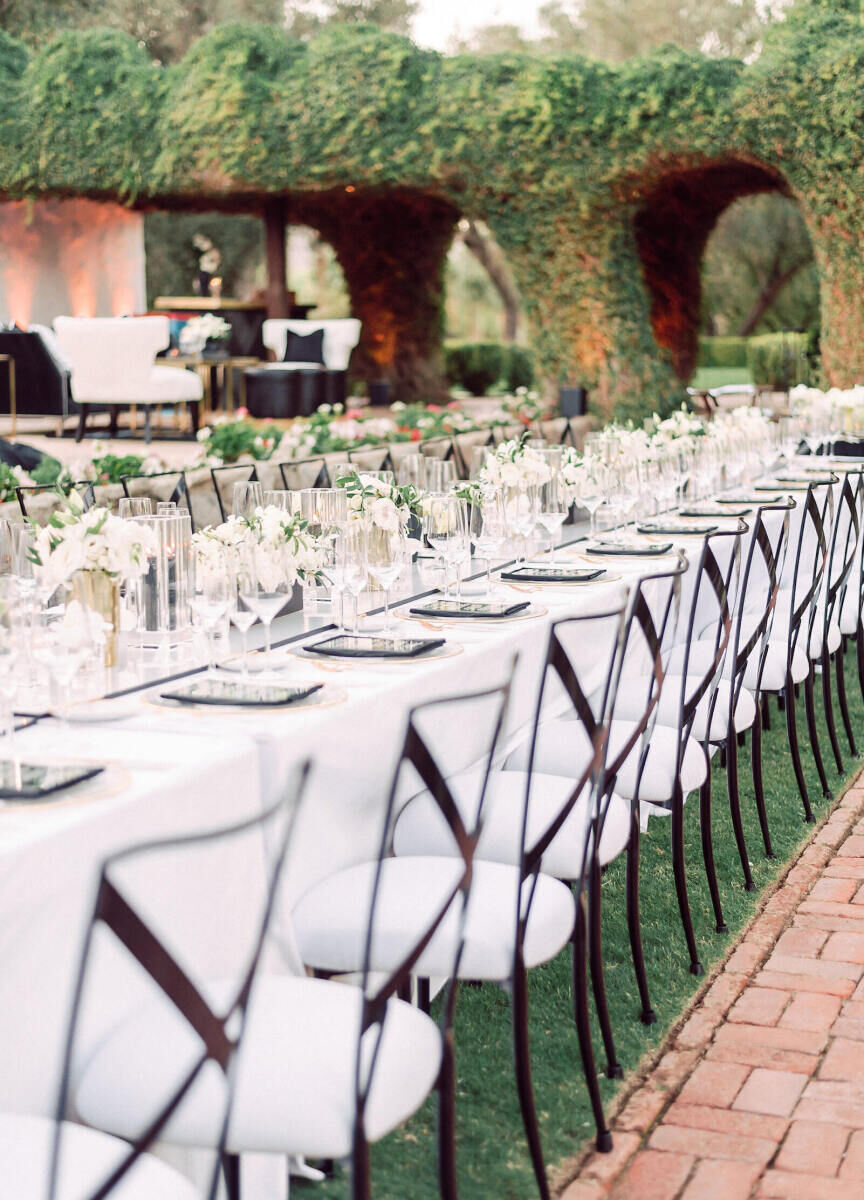 SEO for Wedding Venues: A long reception table with white tablecloths, black chairs with white cushions, and a structure covered in greenery in the background.