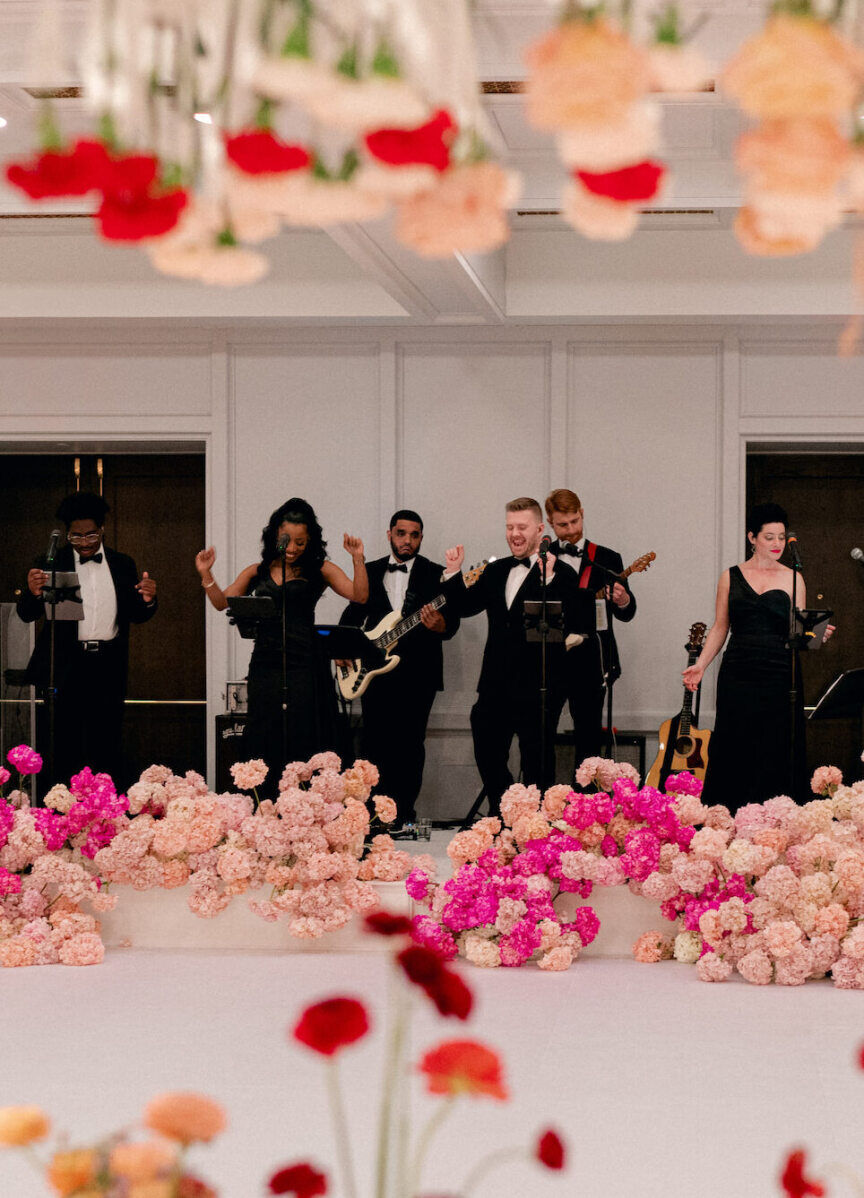 A wedding band performs at a surprise wedding reception, with pink hydrangea spilling over the stage they stand on.