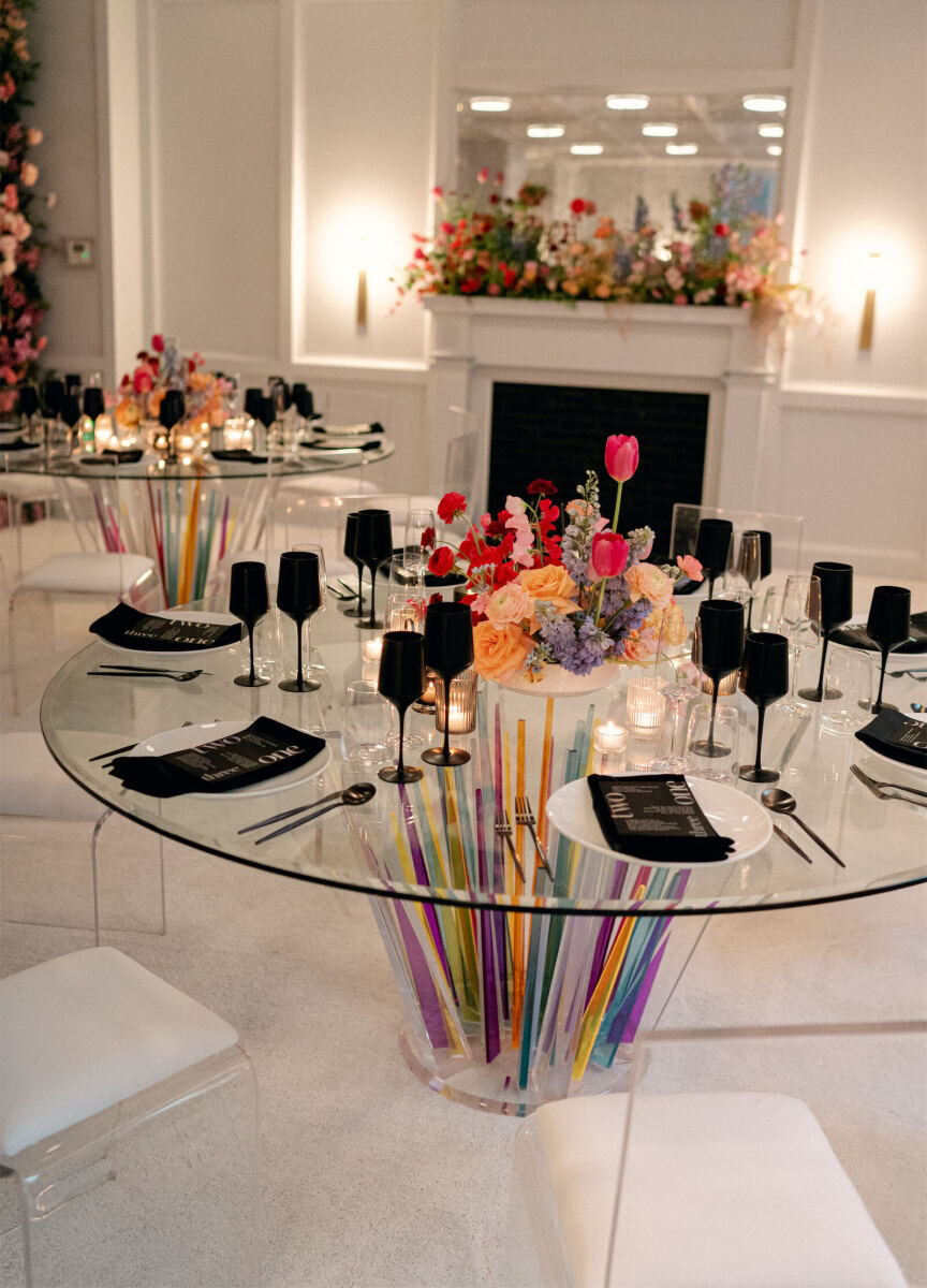 Lots of clear rental pieces were used to set the reception space at this surprise wedding, including this glass table with a colorful base.