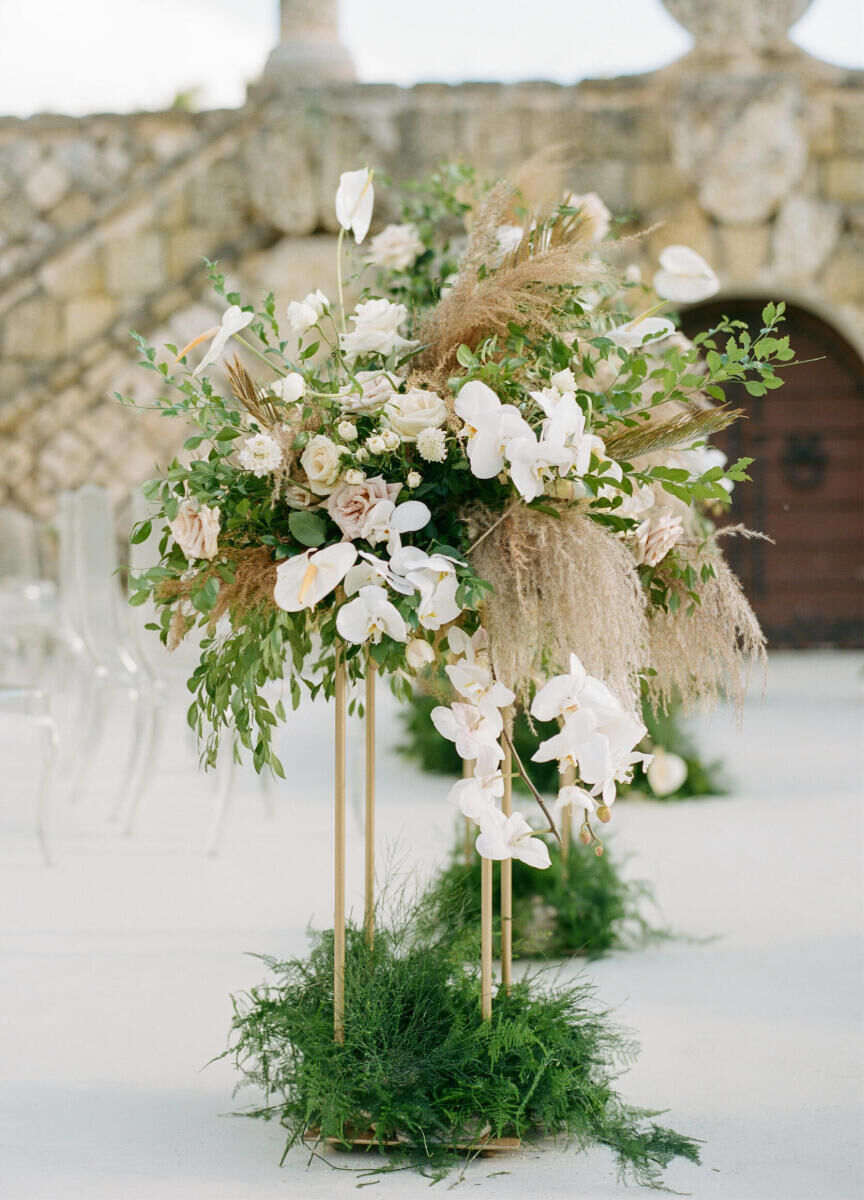 Tropical Wedding:Modern gold framed wedding ceremony aisle pillar adorned with lush greenery and light pink and white blooms.