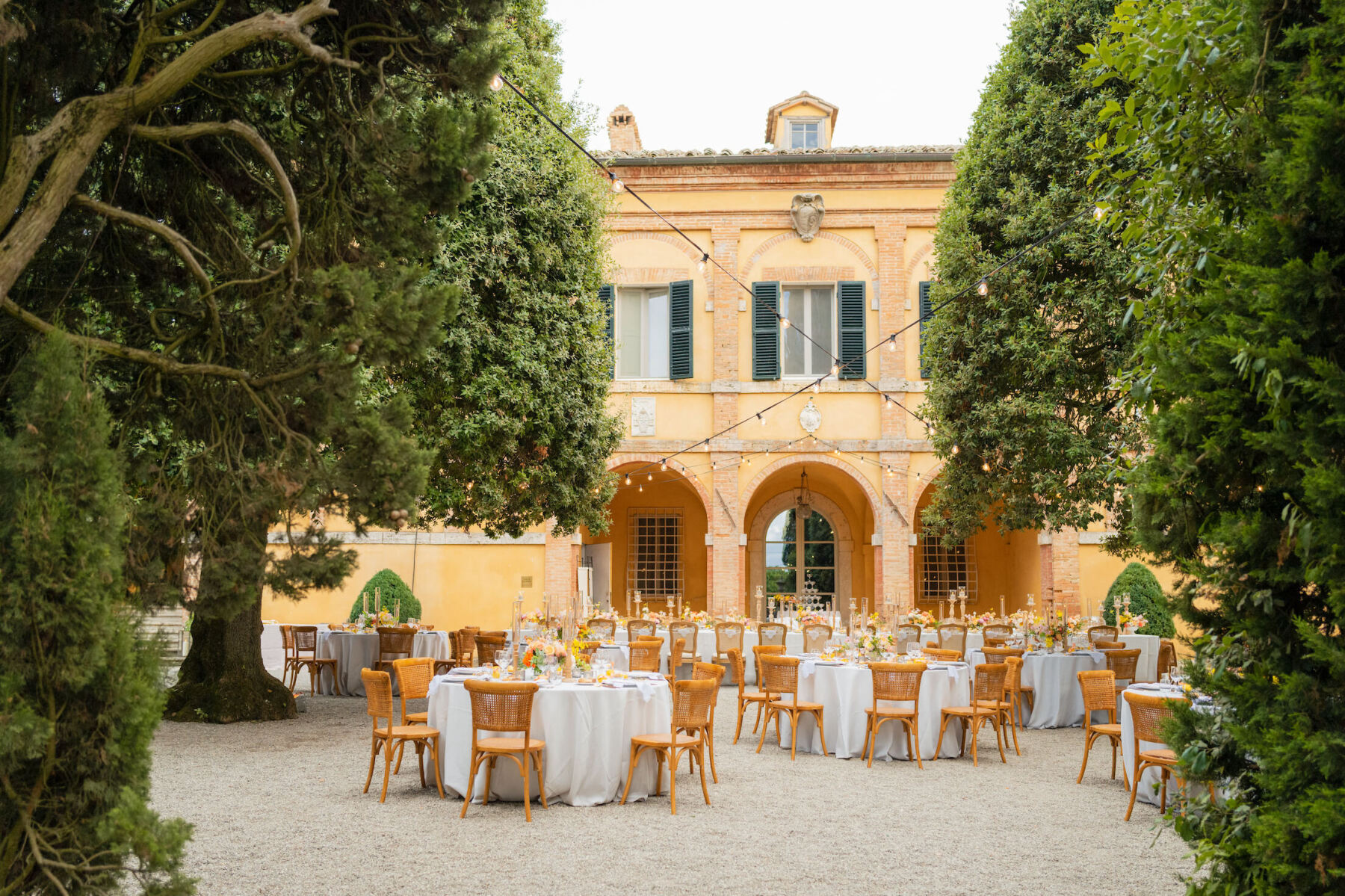An outdoor reception for a Tuscan wedding where tables were set in the courtyard with bistro lights strung overhead.