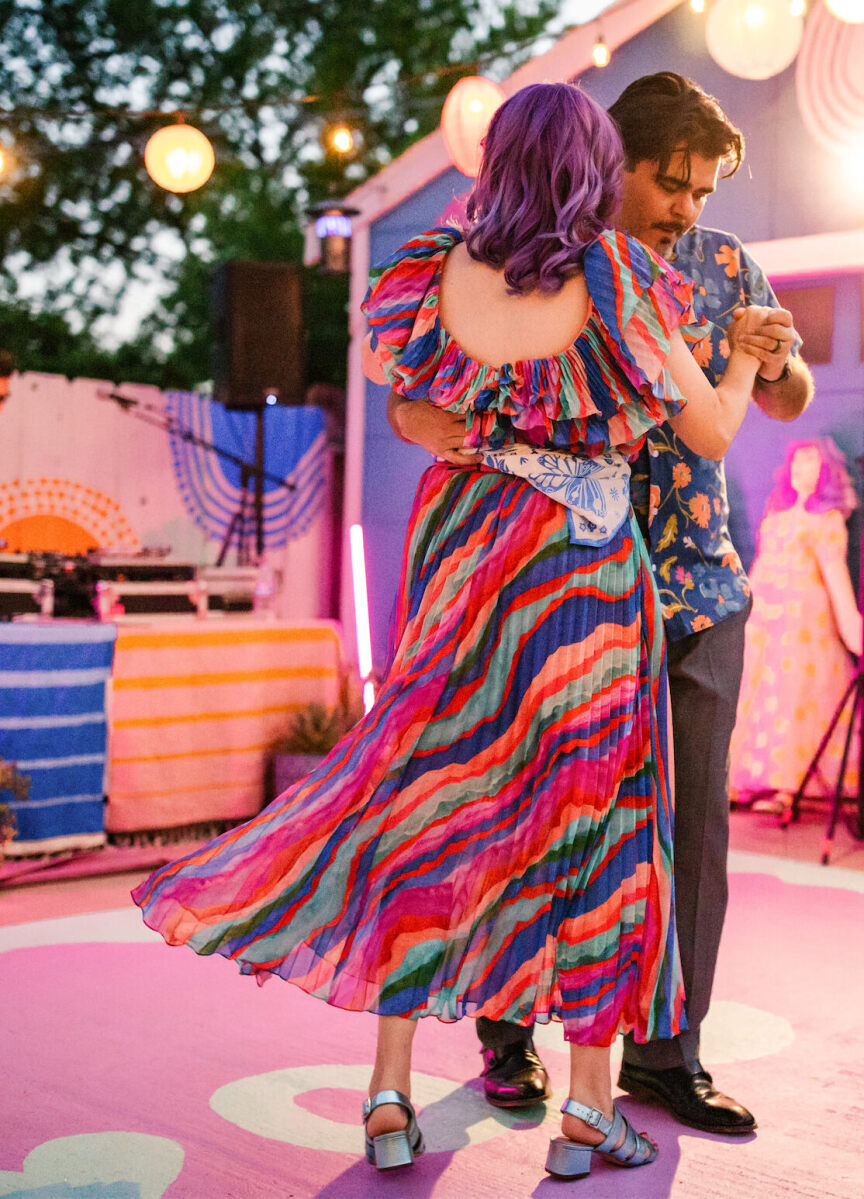 A bride and groom share a first dance on a painted section of concrete in their backyard, where their vibrant outdoor wedding reception took place.