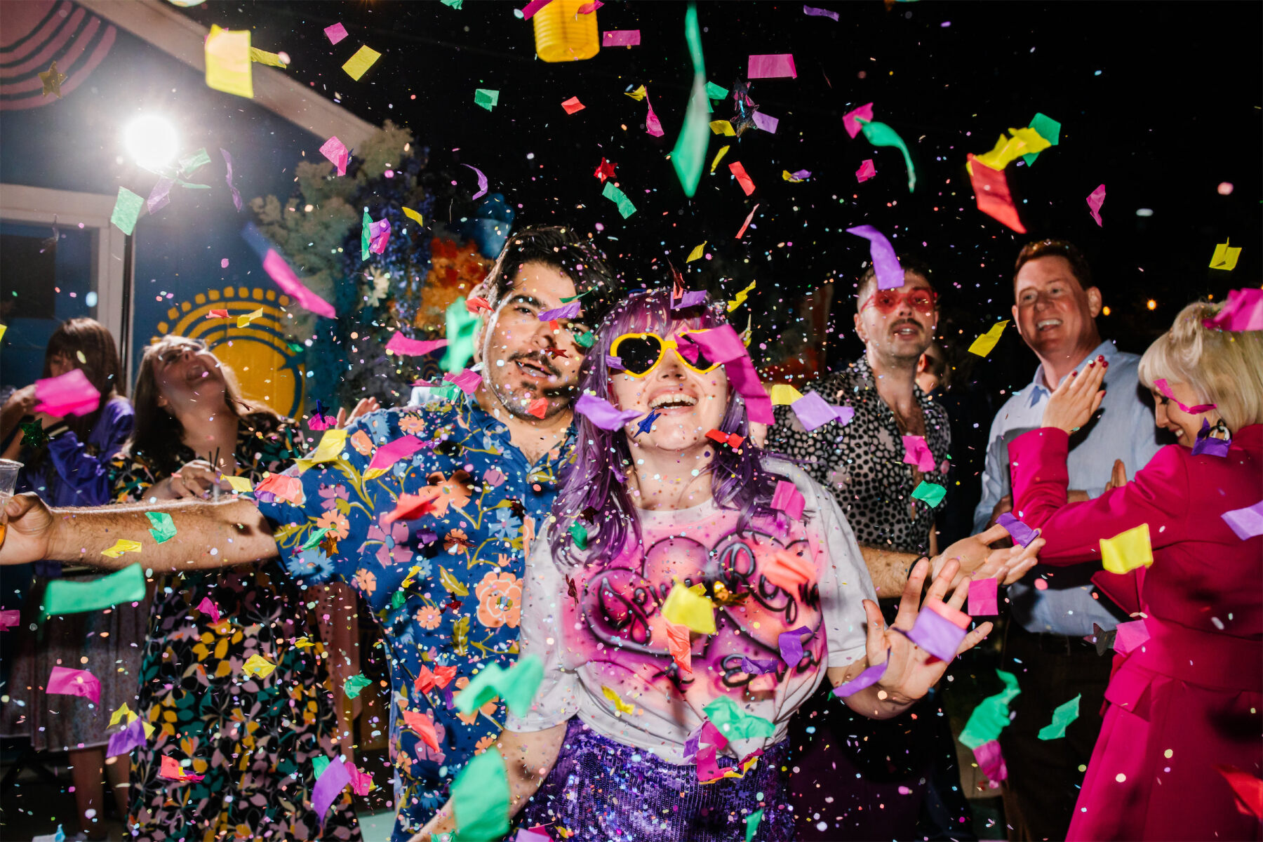 Colorful confetti floats in the air as a pair of newlyweds enjoy the atmosphere of their vibrant outdoor wedding reception.