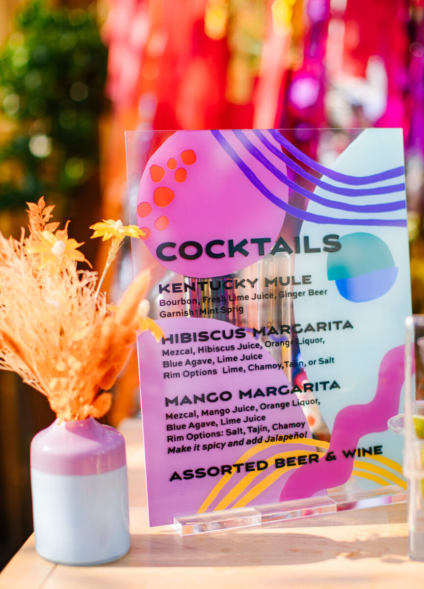 A painted sign outlined the drinks on offer at a vibrant, outdoor wedding reception.