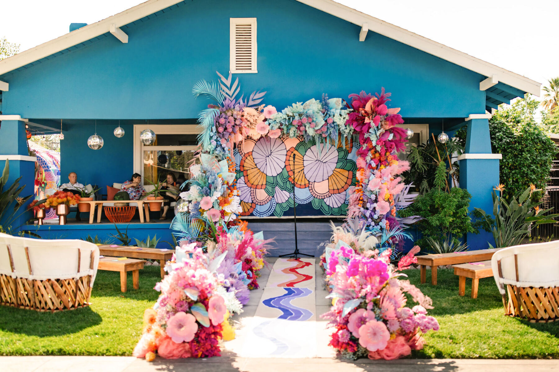At this vibrant outdoor wedding, the couple's teal house was the backdrop, with the ceremony taking place in the front yard, anchored by a colorful floral installation leading to the porch.