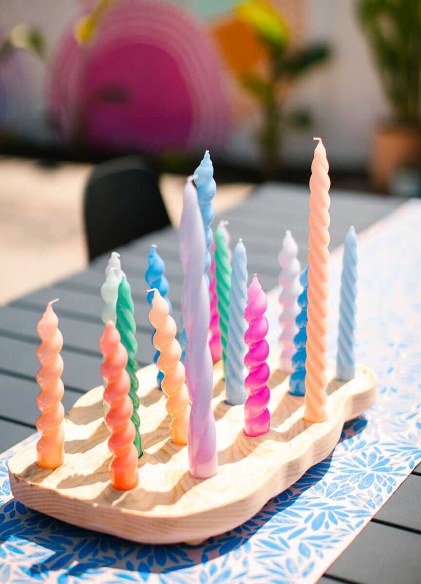 Local artisans crafted some of the decor of this vibrant outdoor wedding, including a curvy wooden board to hold colorful, twisted candles at the reception.