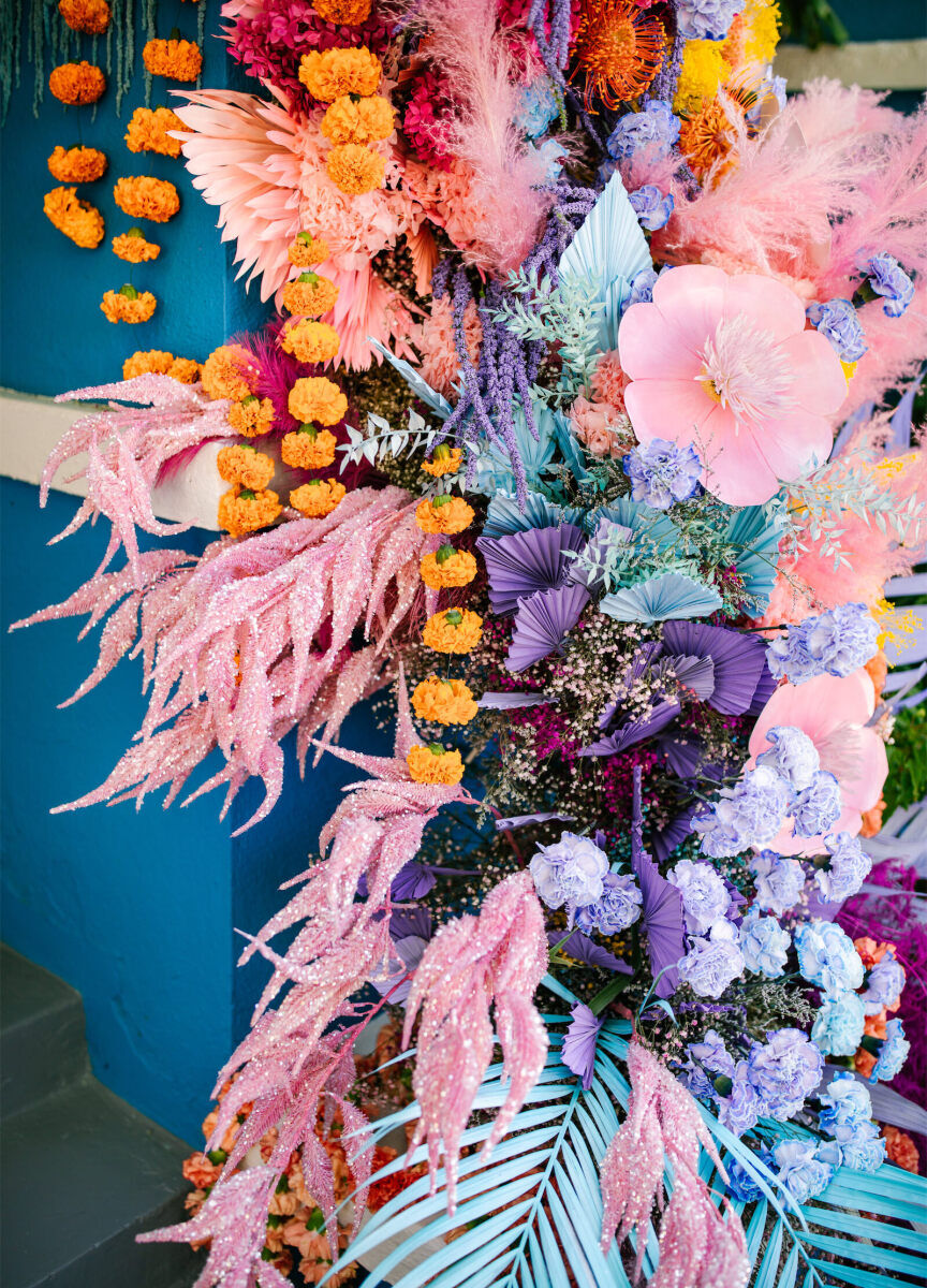 The floral installation that was a focal point of a vibrant outdoor wedding ceremony included a rainbow of blooms—some of which were covered in glitter.